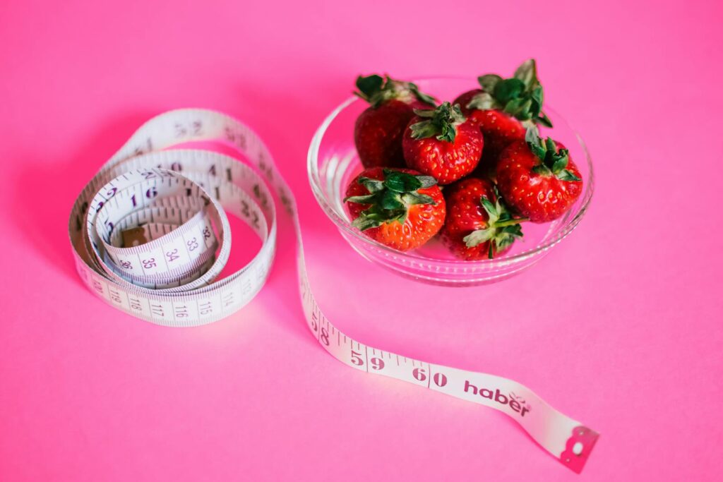 A glass bowl of fresh strawberries paired with a pink measuring tape symbolizes healthy eating.