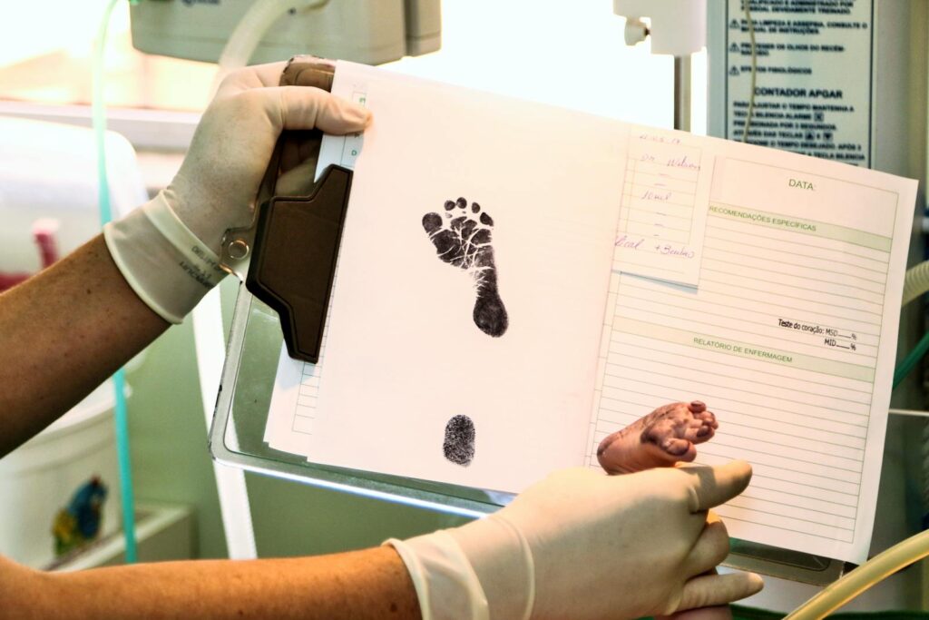 Healthcare professional handling newborn's footprint documentation in a hospital room.