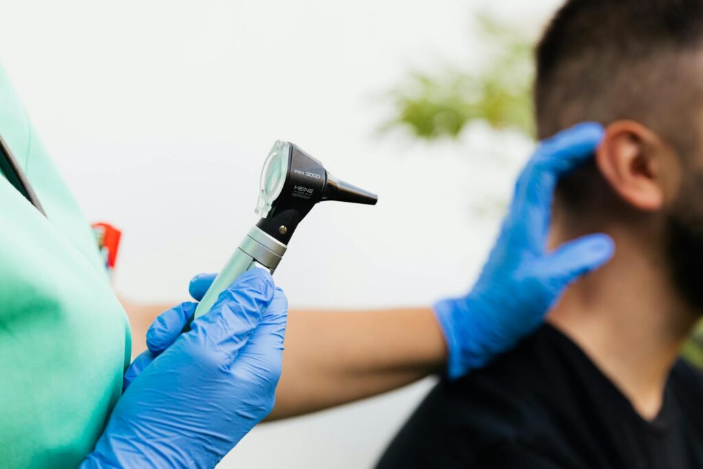 Healthcare professional examining patient's ear with an otoscope in a clinical setting.