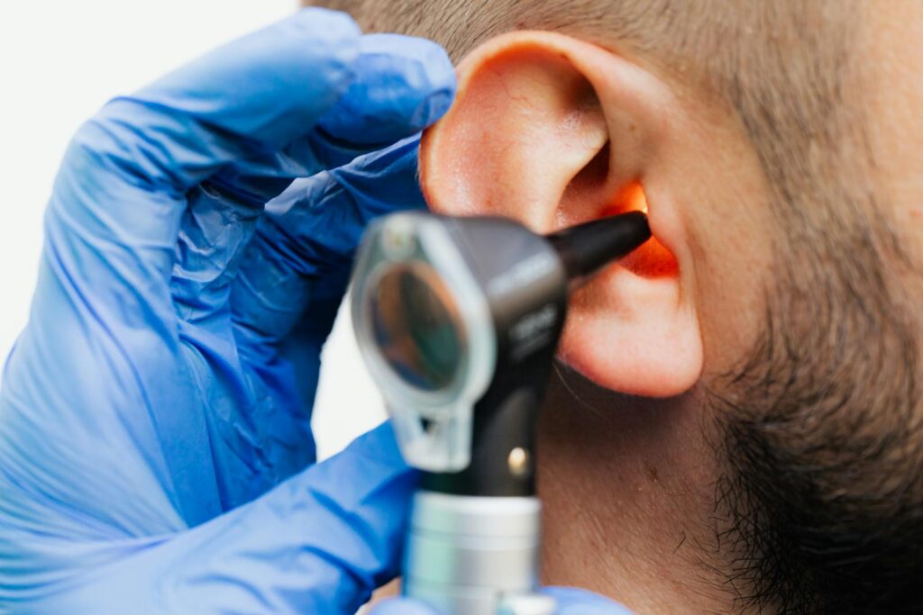 Close-up of a doctor using an otoscope to examine a patient's ear in a clinical setting.