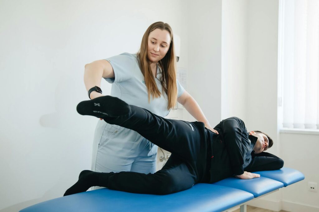 A physiotherapist assists a male patient with leg therapy in a clinic.